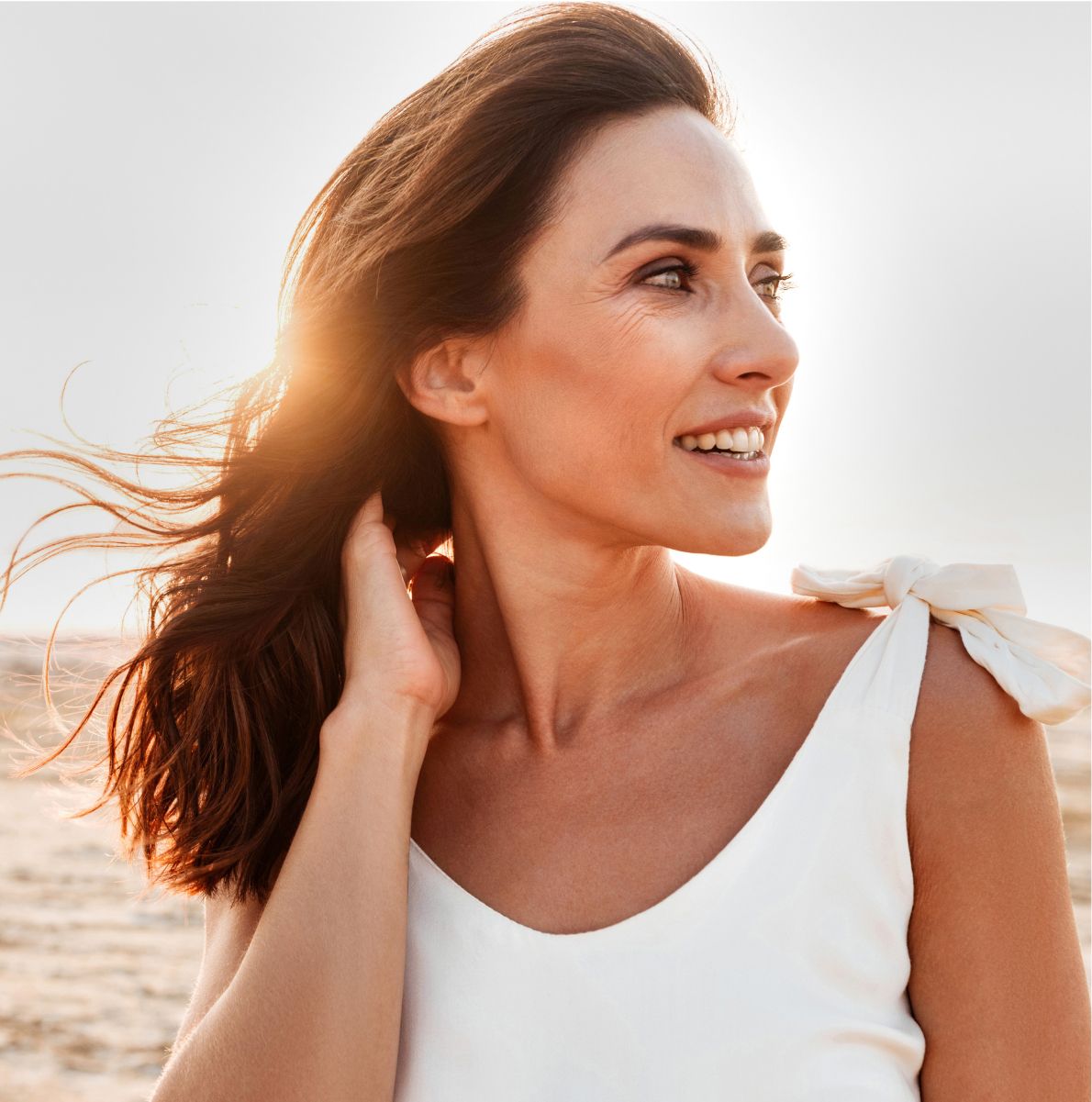 Woman smiling with windblown hair at sunset.
